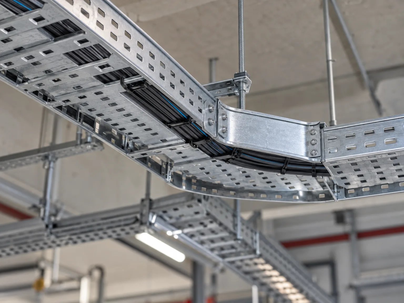 Montierte Kabeltragsysteme mit verlegten Elektrokabeln unter Hallendecke, metallische Konstruktion mit Stahlhalterungen und Verbindungselementen in Industriebet